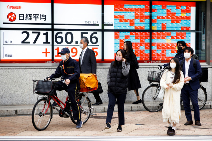Passersby wait at a crossing in front of an electronic board showing Japan's Nikkei average outside a brokerage, in Tokyo