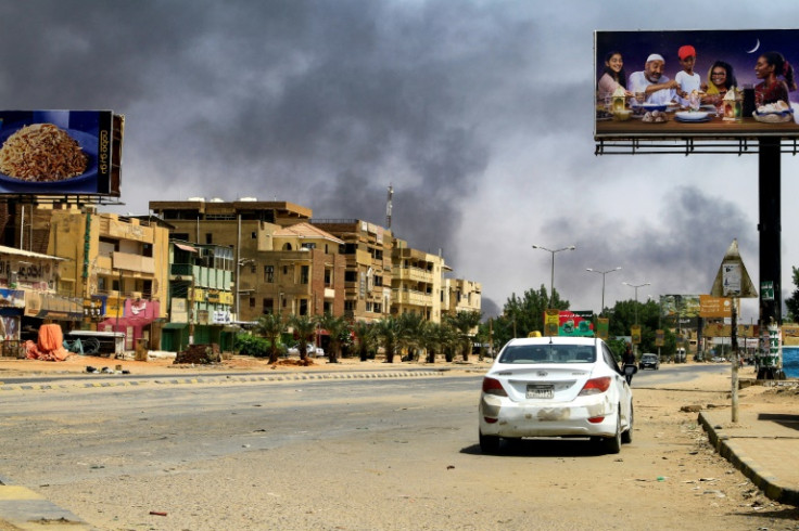 Smoke rises in the background as a car drives along an almost deserted street in Khartoum on April 16