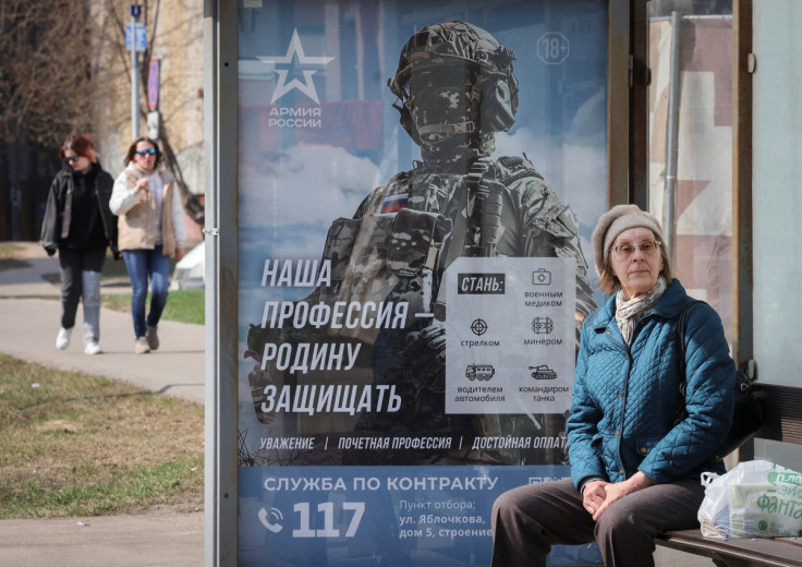 A woman waits at a bus stop next to a poster promoting Russian army service in Moscow