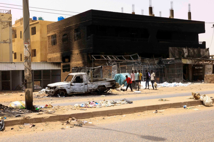 People walk near damaged car and buildings at the central market in Khartoum North