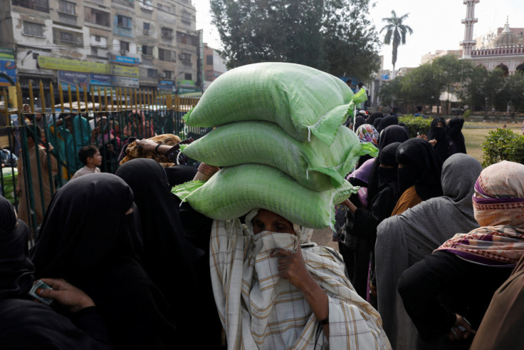 A woman carries sacks of flour on her head, purchased from a truck at subsidised rates, while others stand in queue in Karachi