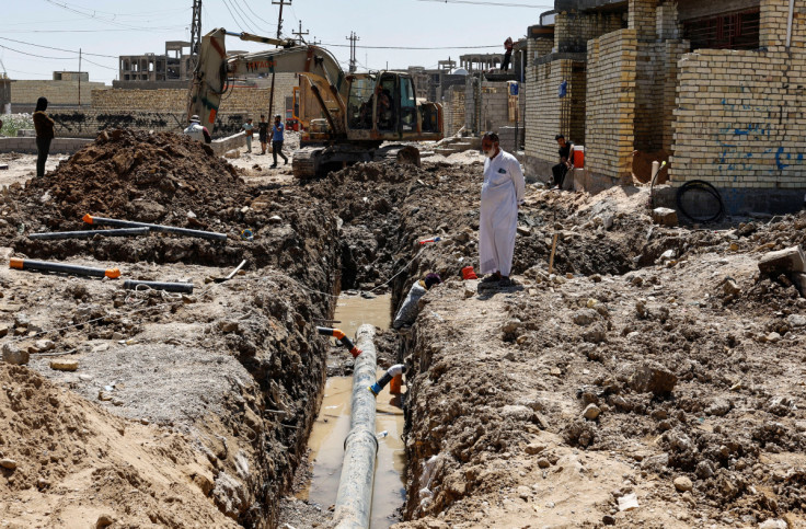 Iraqi workers place a storm sewer pipe into a trench on the outskirts of Sadr city district of Baghdad