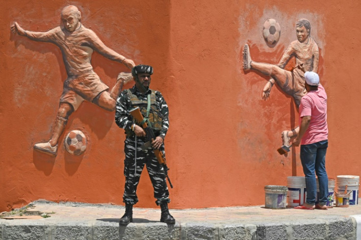 An Indian paramilitary trooper stands guard next to an artist giving final touches to a mural along a street ahead of the G20 meeting in Srinagar