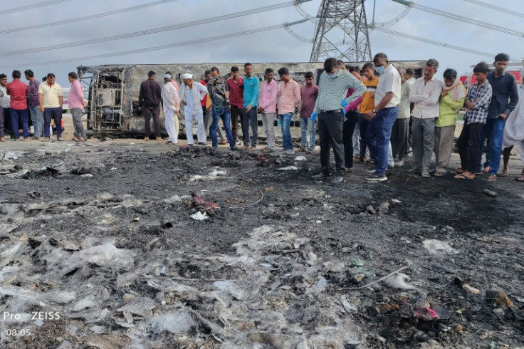 People gather next to the remains of a bus (background) that overturned and caught fire in western India