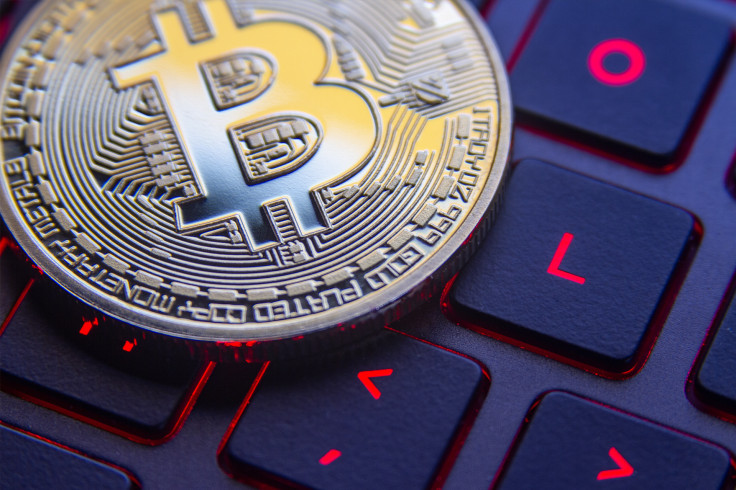 Bitcoin on laptop keyboard with red-lit keys and screen reflection.
