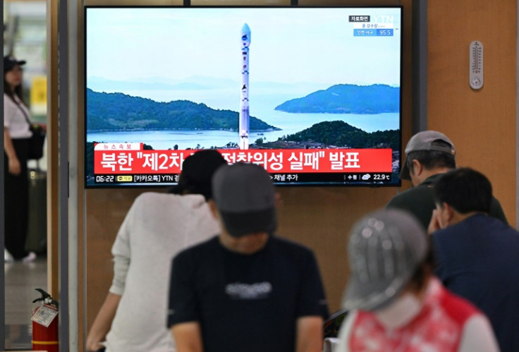 People watch a television screen showing a news broadcast with file footage of a North Korean satellite-carrying rocket launch, at a railway station in Seoul in August 2023