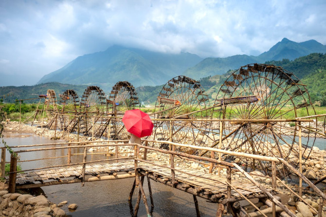 Red umbrella on footbridge above river with water mills