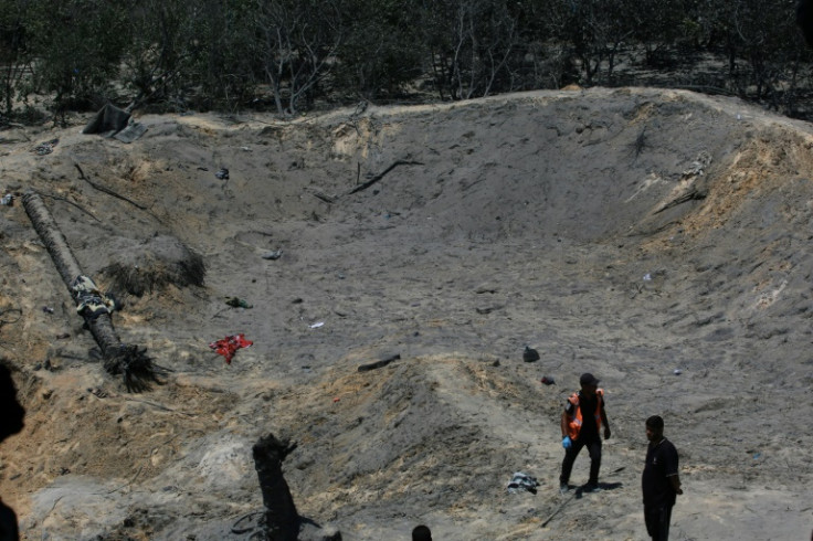 Palestinians look at a huge crater in the sand following an Israeli military strike on the al-Mawasi camp for displaced people in the Gaza Strip
