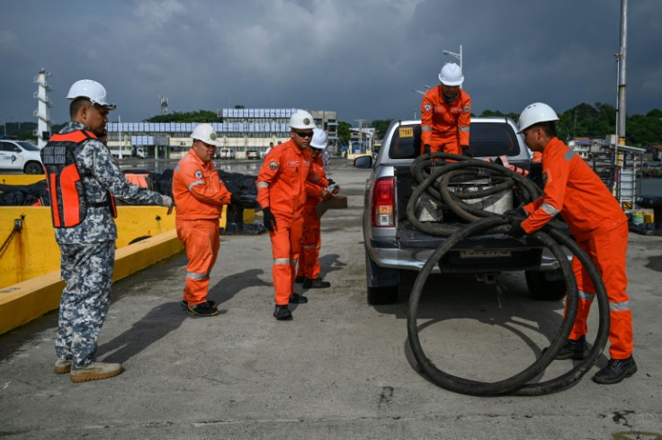 Coast guard personnel carry a suction hose for deployment at a port in Limay
