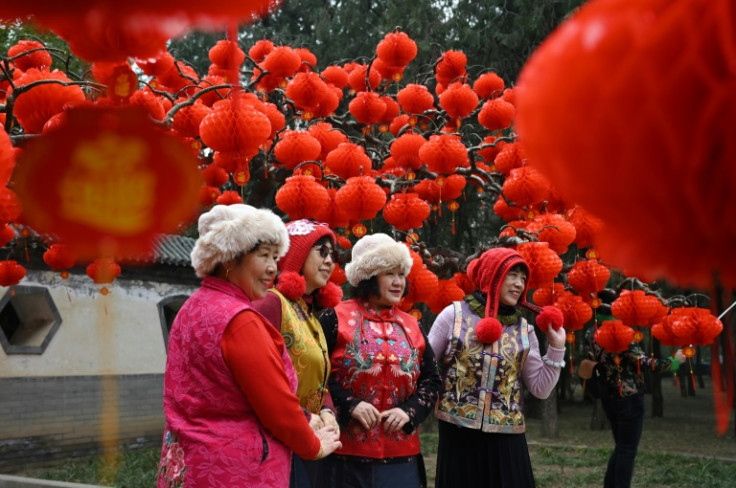 A group of women pose for photos under decorations for a temple fair ahead of Lunar New Year celebrations in Beijing