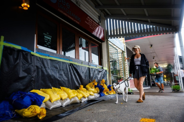 A woman and her dog walk past a sandbagged store in Brisbane on March 6, 2025, as tropical cyclone Alfred approaches. The outer fringe of a tropical cyclone started whipping eastern Australia on March 6, bringing drenching rains and record-breaking waves
